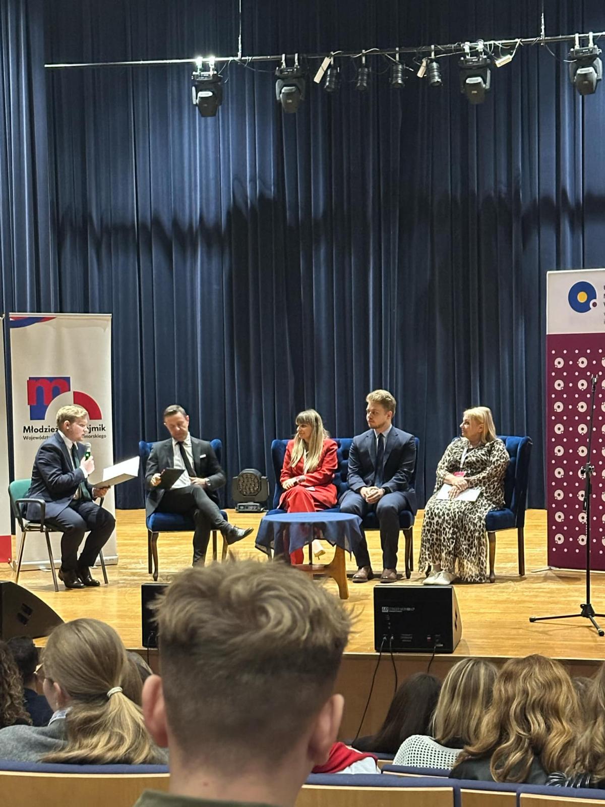 Pięć osób siedzi na scenie i prowadzi rozmowę