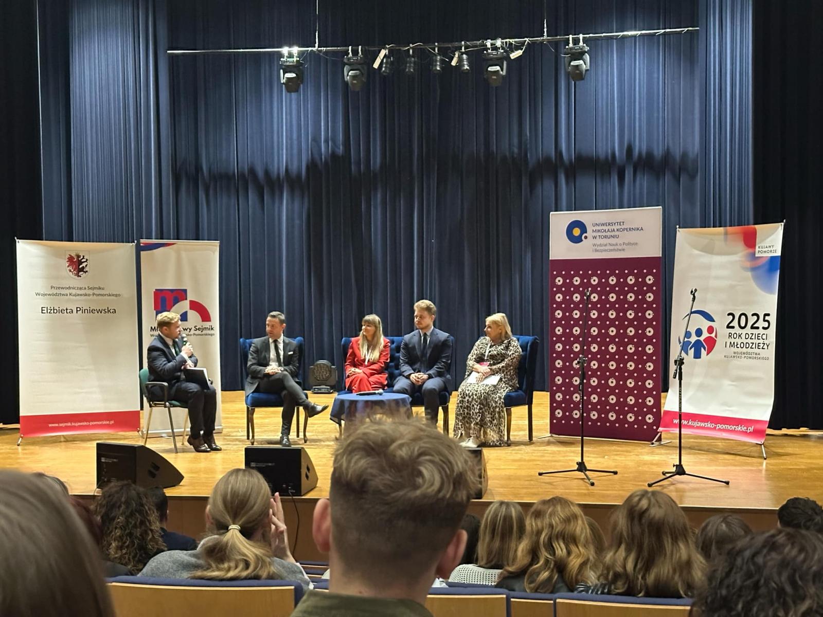 Pięć osób siedzi na scenie i prowadzi rozmowę