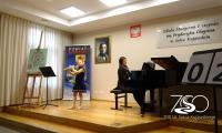 Występ młodej flecistki z akompaniatorem przy fortepianie. Na zdjęciu logo siedemsetlecia.