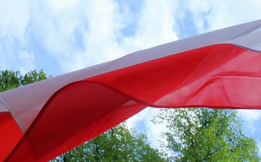 Biało-czerwona flaga na tle nieba i drzew.