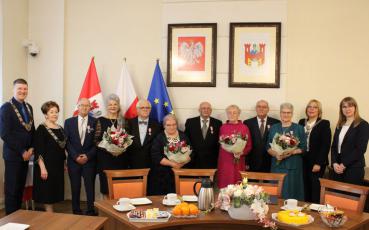 Jubilaci wraz z przedstaicielami samorządu. Panie trzymają bukiety kwiatów. Z tyłu flagi oraz polskie godło i herb Solca Kujawskiego.