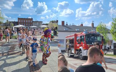 Dzieci bawiące się na festynie z klownem i wóz strażacki.