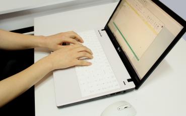 Dłonie na laptopie leżącym na biurku.