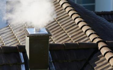 Dach domu z kominem, z którego wydobywa się dym.