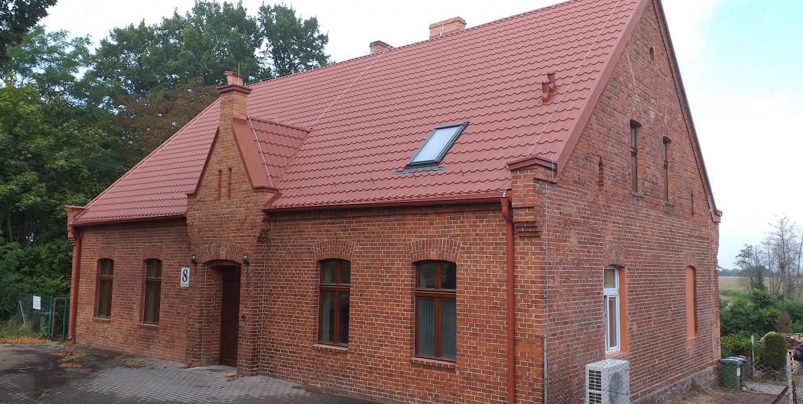 Budynek świetlicy z czerwonej cegły i z nowym pokryciem dachowym.