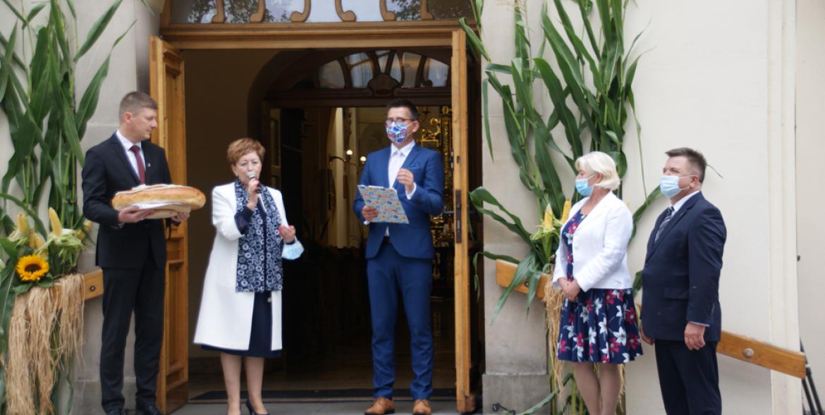 Burmistrz i przewodniczący rady, starostowie dożynek i prowadzący ceremoniał dożynkowy przed kościołem.