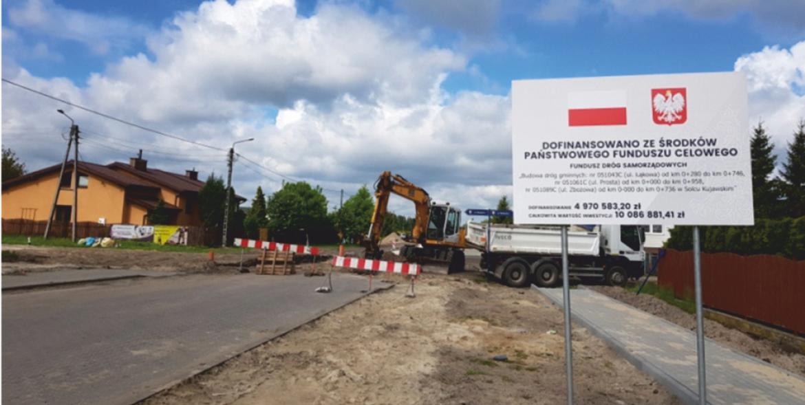 Ulica Zbożowa w trakcie budowy. Na pierwszym planie tablica informująca o dotacji z Funduszu Dróg Samorządowych.