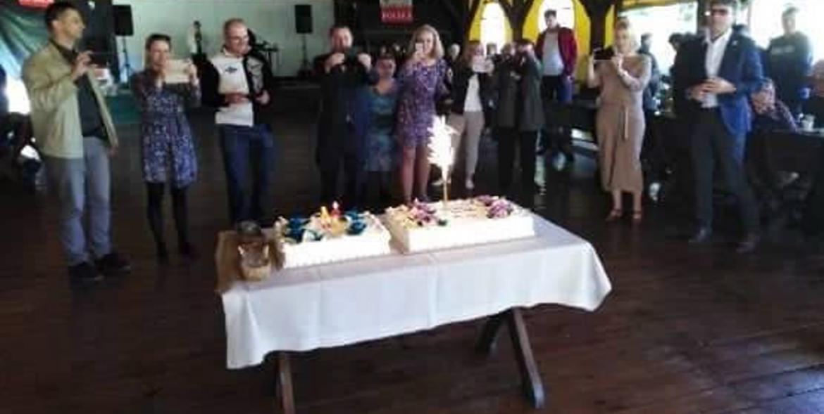 Uczestnicy spotkania oraz na pierwszym planie, na stole, torty urodzinowe.