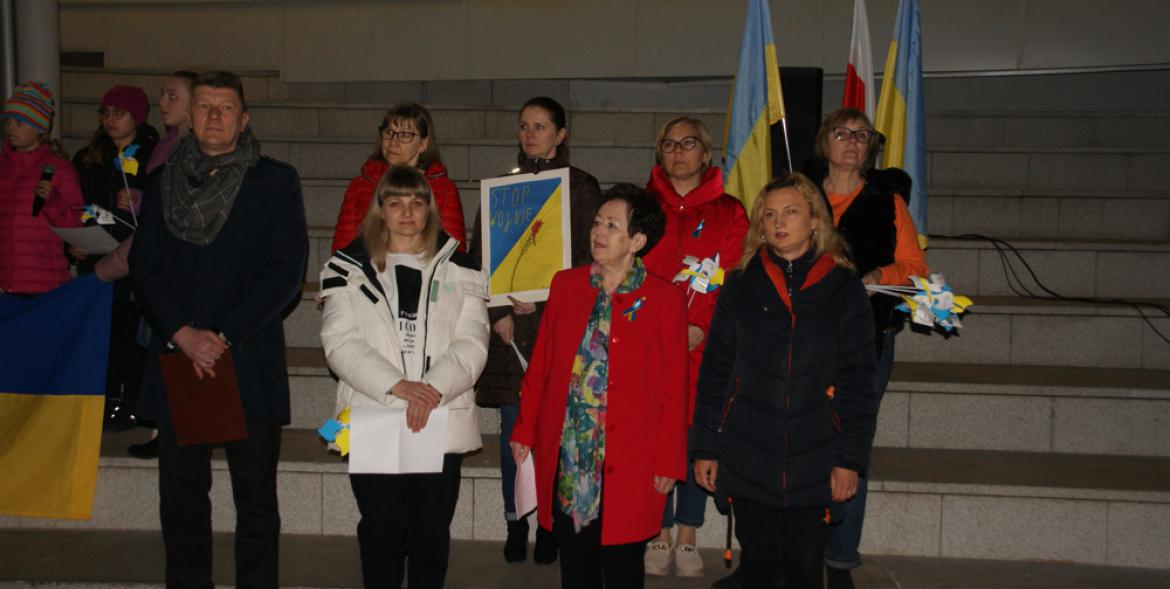 Przedstawiciele samorządu wraz z ukraińskimi uchodźcami stoją przed dworcem.