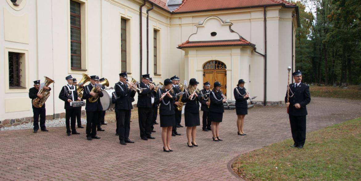 Przed kościołem gra strażacka orkiestra dęta.