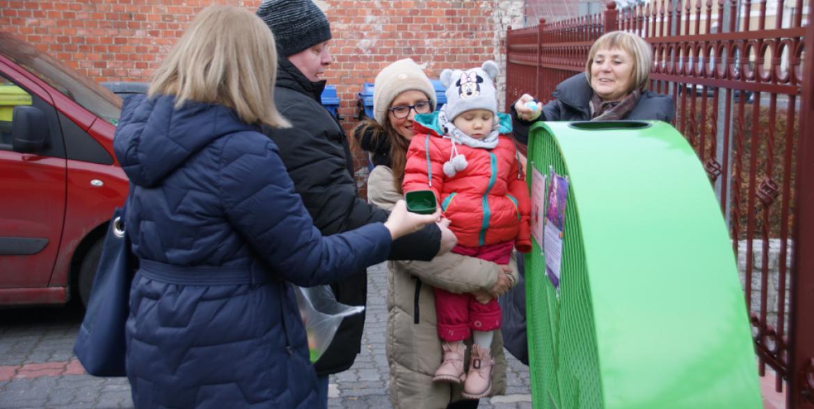 Pierwsze nakrętki trafiły do pojemnika. Lenka z mamą i pracownicy urzędu.