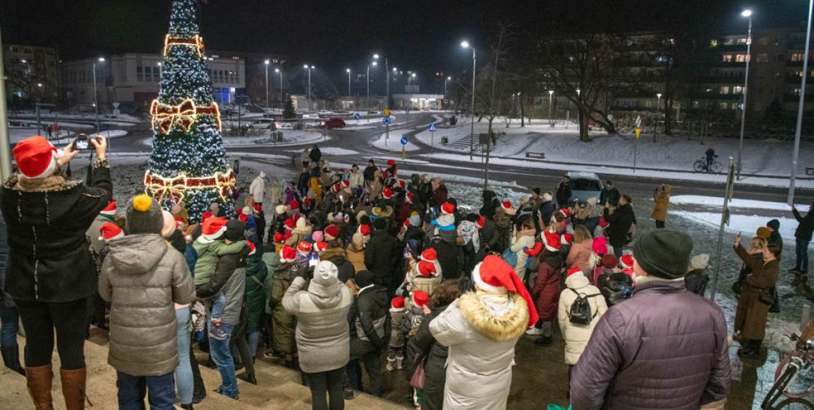 Mieszkańcy koło rożświetlonej choinki przy dworcu kolejowym.