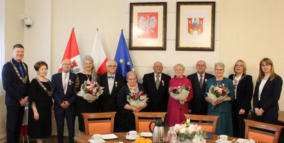 Jubilaci wraz z przedstaicielami samorządu. Panie trzymają bukiety kwiatów. Z tyłu flagi oraz polskie godło i herb Solca Kujawskiego.