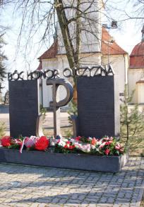 Pomnik Armii Krajowej. Po obu stronach symbolu Polski walczącej(kotwicy) dwie pionowe płyty. Na górze pomnika napis Bóg Honor Ojczyzna.